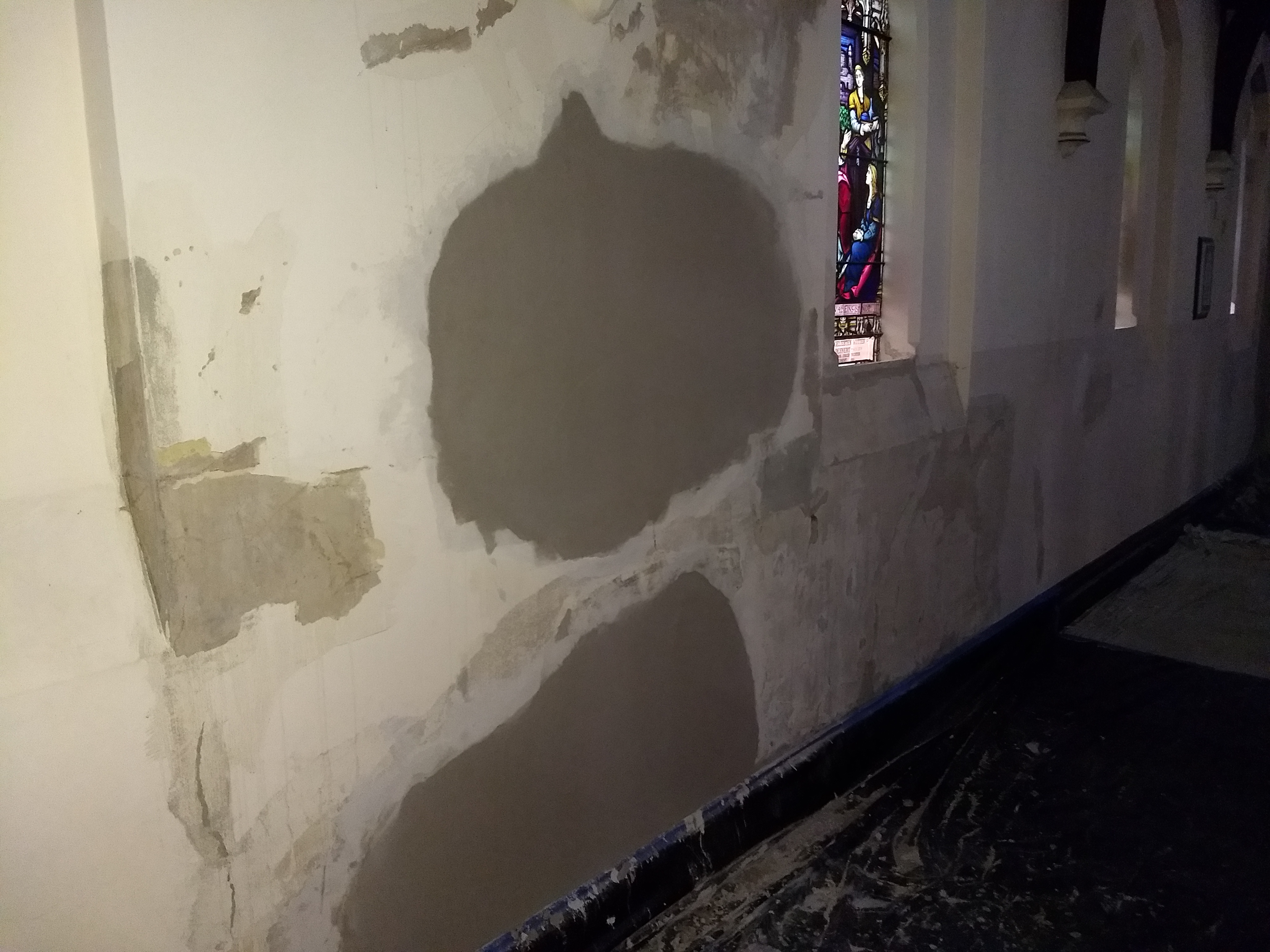 Broad mineral plaster repair zones along the church wall